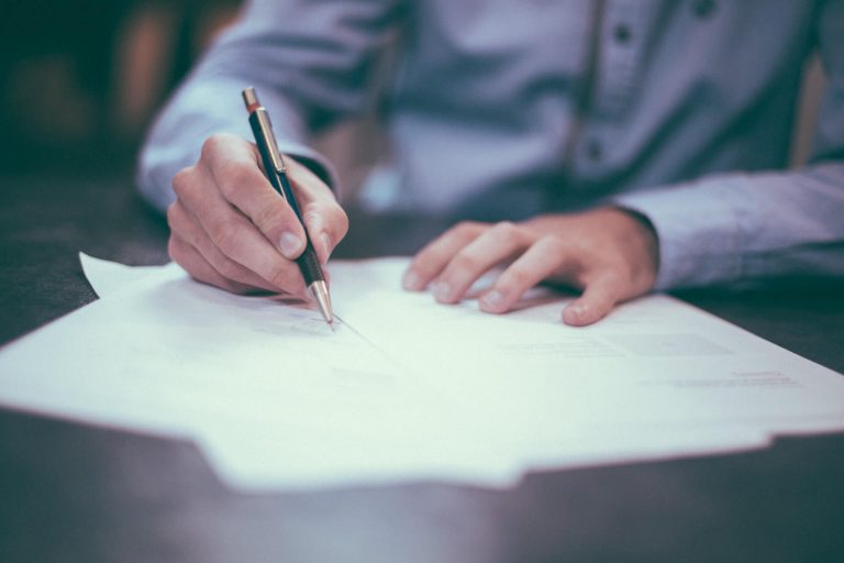 Notario Público en Mazatlán asesorando a una persona con vestimenta formal mientras firma documentos legales en una notaría.